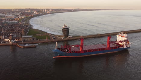 Aerial-view-of-a-cargo-ship-entering-Aberdeen-harbour-at-sunset,-Aberdeenshire,-Scotland,-UK