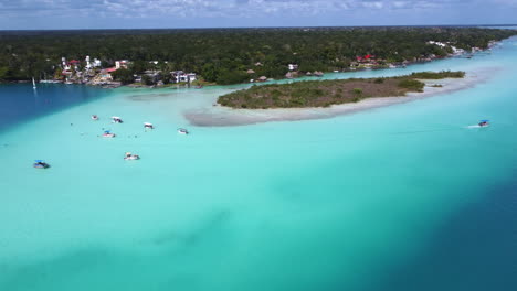 Aerial-panning-shot-of-paradise-resort-at-the-sunny-Bacalar-lagoon,-in-Mexico-with-tropical-forest-in-the-background