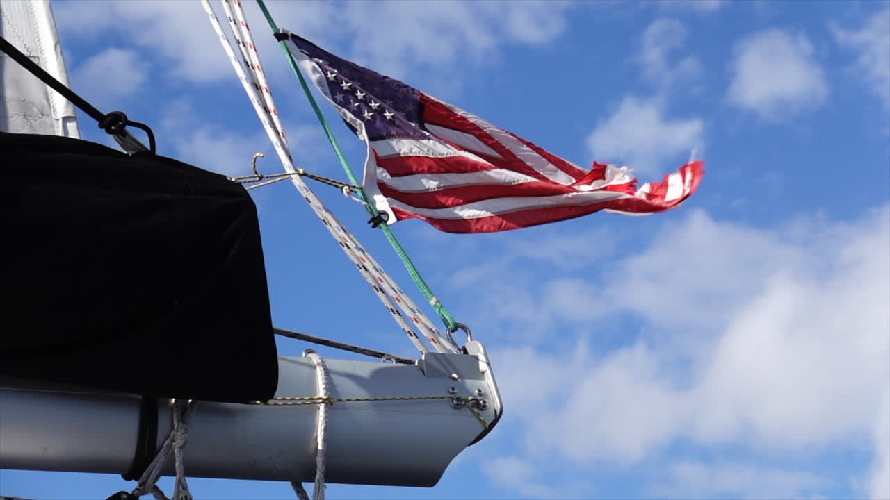 American flag flies in the wind on the boom of a sailboat with speckled clouds in the background