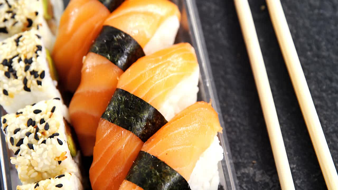 Plastbakke med forskellige sushi-ruller og laks