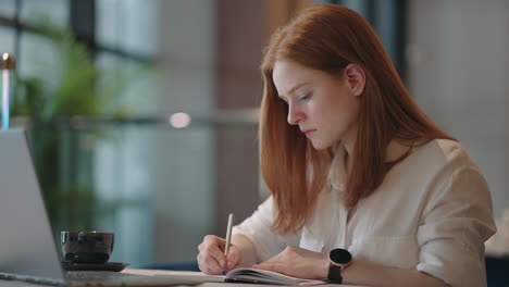 young female writer is working alone at home making notes in book journalist freelancer is writing