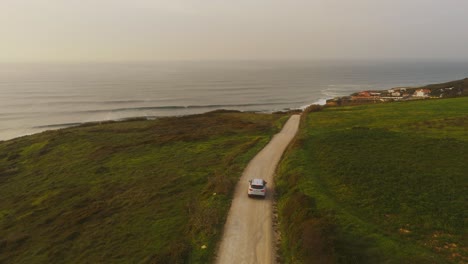 Vista-Aérea-De-Un-Suv-Moderno-Conduciendo-Por-La-Costa-De-Magoito,-Puesta-De-Sol-En-Portugal