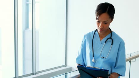 Female-doctor-looking-at-clipboard-in-corridor