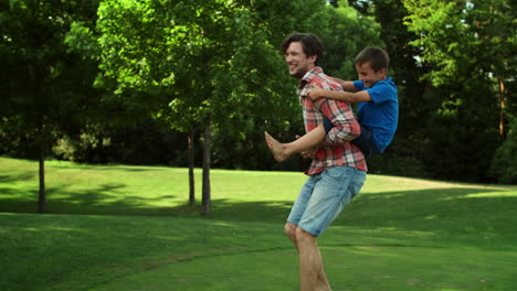 Man-running-in-field-with-boy-on-back.-Father-giving-son-piggyback-riding