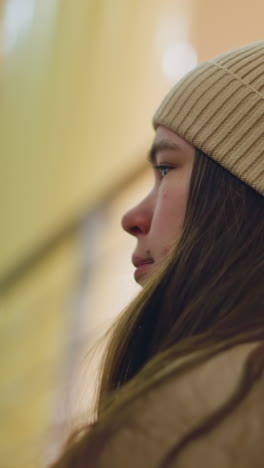 perfil lateral de primer plano de una joven que lleva un gorro de costillas marrones, con el cabello largo descansando en su hombro. momento contemplativo, con una suave iluminación interior que crea una atmósfera cálida. fondo borroso