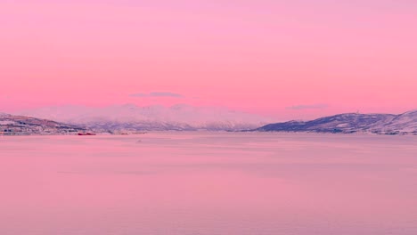 wide view of the sea in tromso norway, with pink hues and snow covered mountains in the distance