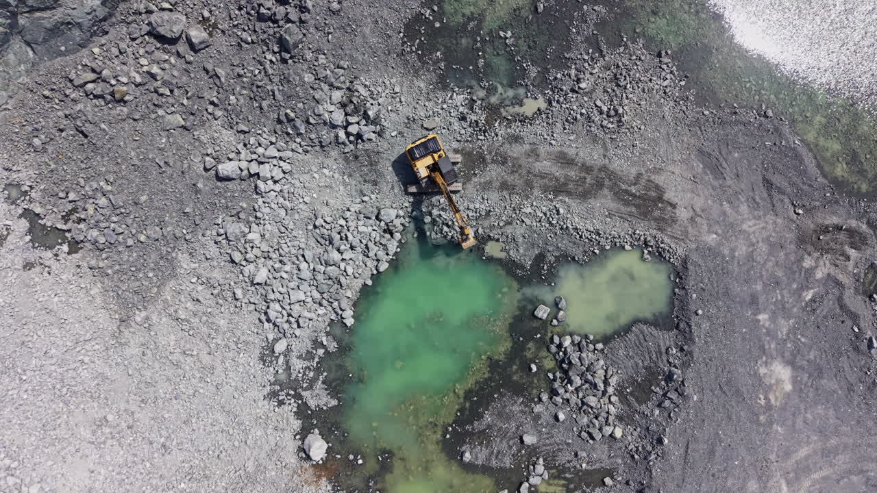Granite quarry site with excavator working and water pools present in the landscape during daylight hours