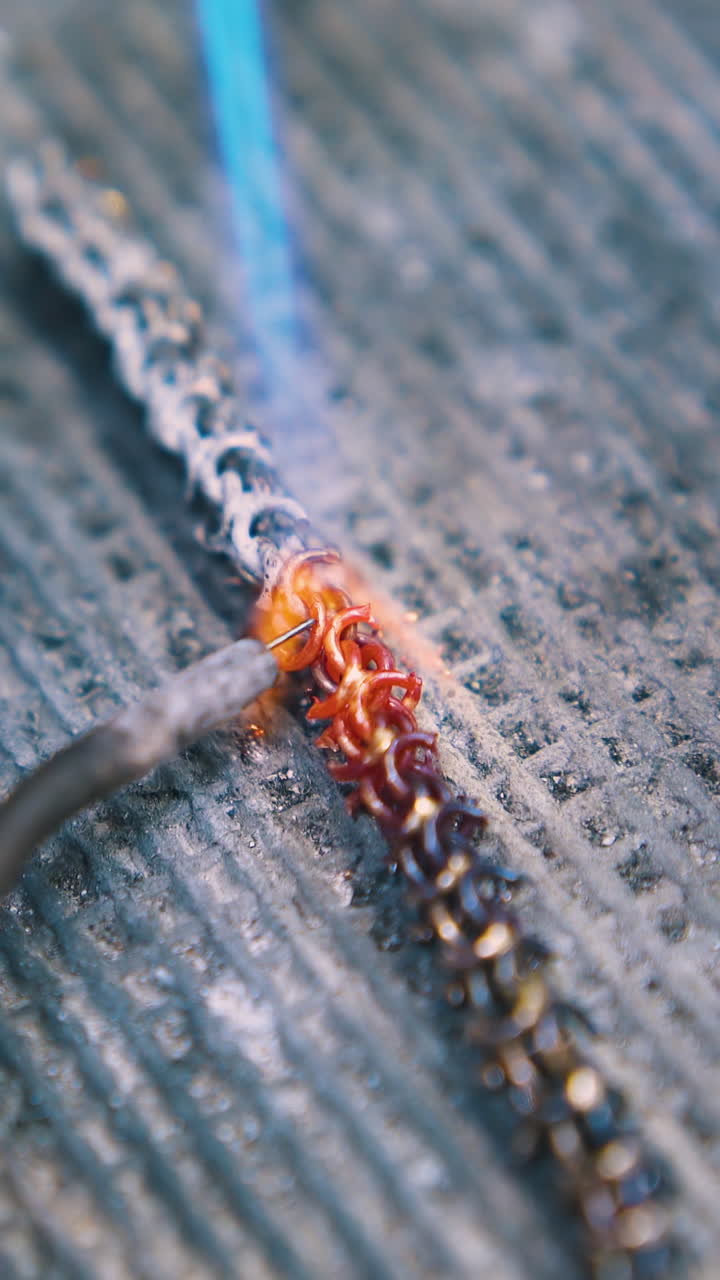 CU: professional jeweler processes decorative gold metal chain with gas burner on fireproof asbestos sheet close view