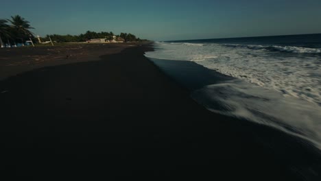 drone flying on foamy waves at the black sand coastline of monterrico beach in guatemala