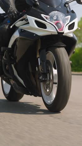 man adventurer drives modern motorcycle along empty outskirts highway past green trees on sides on sunny day slow motion close view