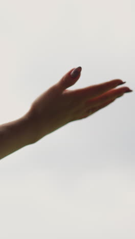 stretched hand of young woman with long nails and open palm under warm rain drops against grey cloudy sky on nasty day close view slow motion