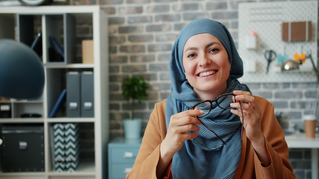 Smiling Woman in Hijab Holding Glasses in Modern Office