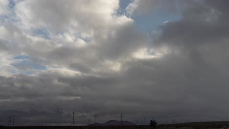 Cloudscape-over-the-Mojave-Desert-landscape,-mountains-and-electrical-transmission-towers---static,-wide-angle-time-lapse