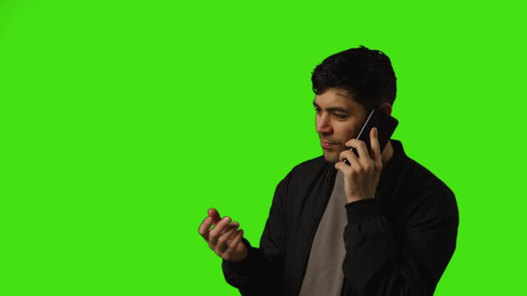 Young Man Talking On Mobile Phone Standing Against Green Screen Studio Background