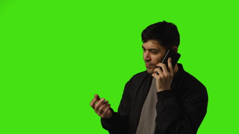 Young-Man-Talking-On-Mobile-Phone-Standing-Against-Green-Screen-Studio-Background