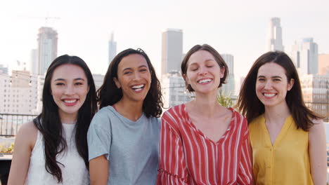 portrait of female friends gathered on rooftop terrace for party with city skyline in background