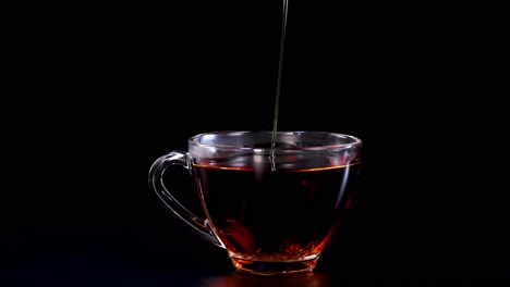 honey streams into a glass cup of tea, creating a soothing visual against a dark backdrop