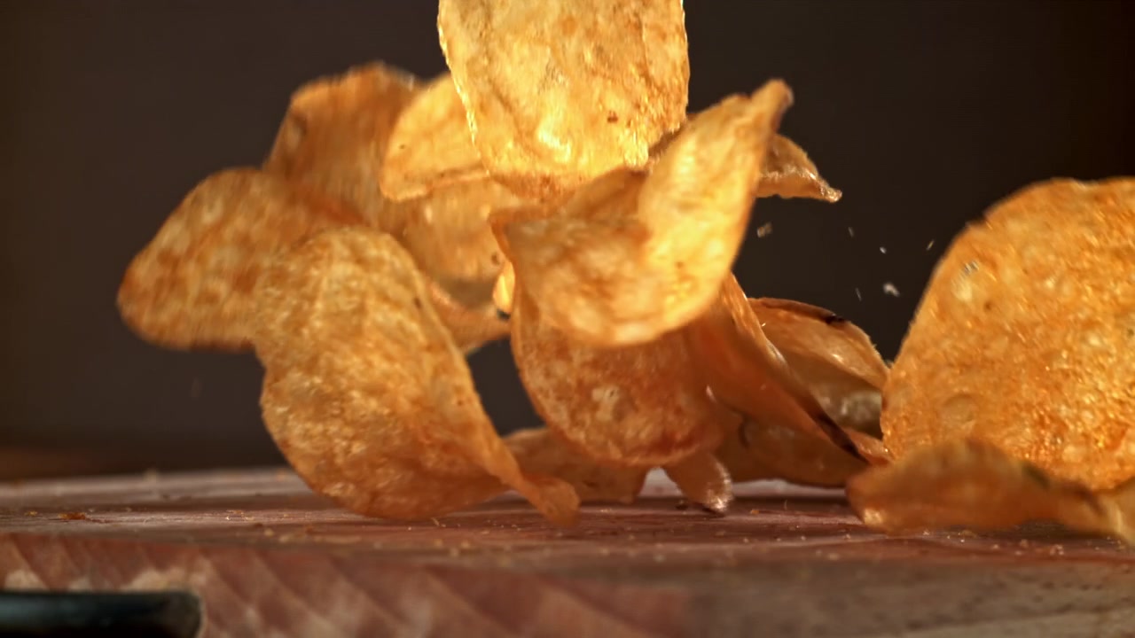 Crispy Potato Chips Falling onto a Wooden Surface in Slow Motion