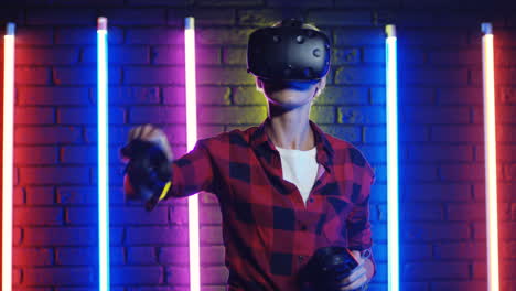 young woman in vr glasses and using joystick while playing a virtual reality game in a room with colorful neon lamps on the wall 3