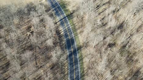 drone aerial view of a red car driving on a road surrounded by woods in early spring in pataskala ohio