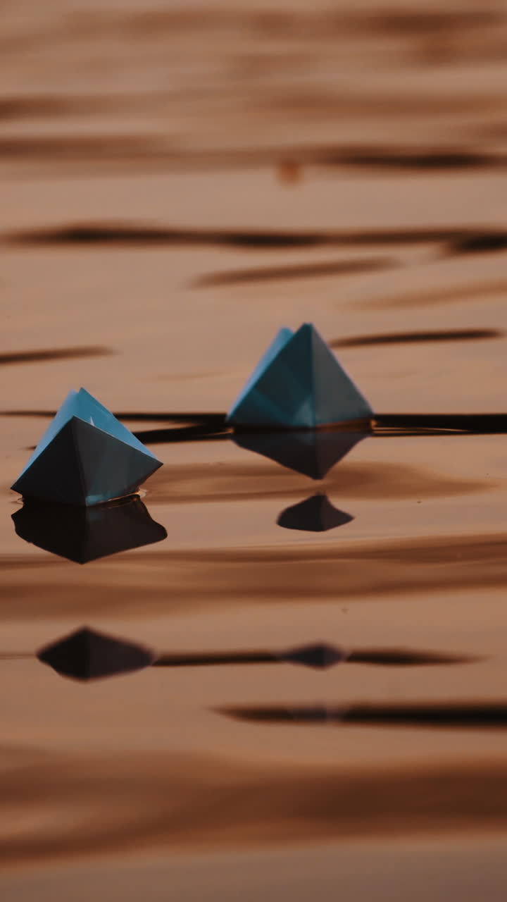 Evening water background and two paper boats swimming. Homemade origami ships floating on beautiful water surface. Vertical video