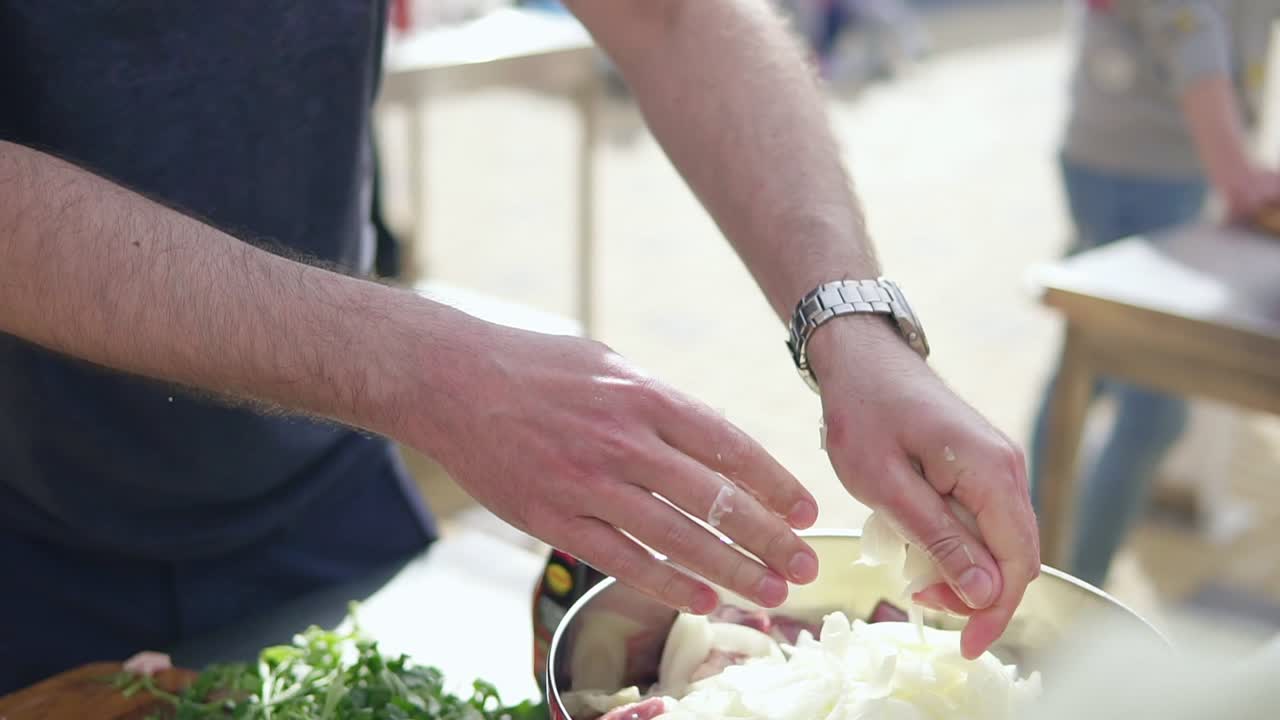 남자는 금속 그 ⁇ 에 고기 조각과 향신료와 양파를  ⁇ 고 있습니다. 밖의 나무 표면. 바베큐 시간. 4k로 촬영