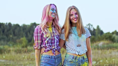 portrait shot of the two happy and beautiful blonde young girls looking at each other, hugging and smiling to the camera, best friends having fun at the holi holiday