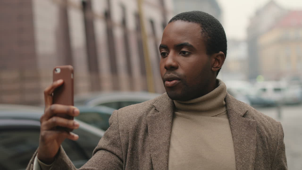 Close-up view of young African American businessman wearing coat  and talking on a video call in the street in autumn