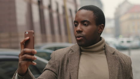 close-up view of young african american businessman wearing coat  and talking on a video call in the street in autumn