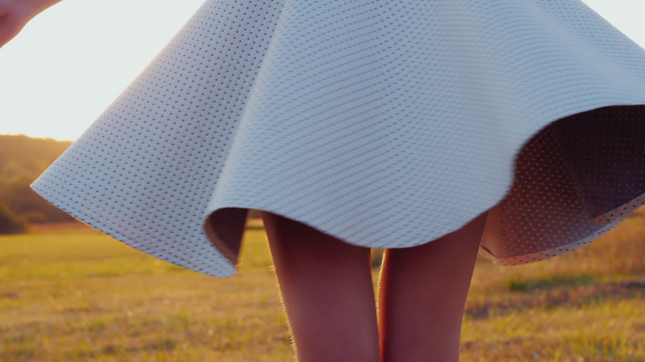 가벼운 치마를 입은 젊은 날씬한 여성이 일몰 슬로우 모션 4k 비디오에서 초원에서 회전하고 있습니다.