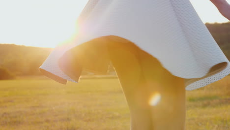 a young slim woman in a light skirt is spinning in a meadow at sunset slow motion 4k video