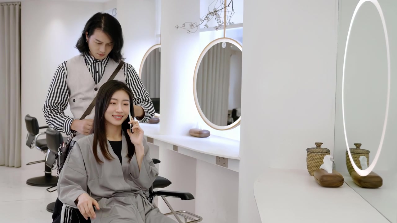 Young female client businesswoman talking on mobile phone while getting trendy haircut from designer hair stylist, hairdresser hairdressing scissors, grooming comb hairstyle salon barbershop