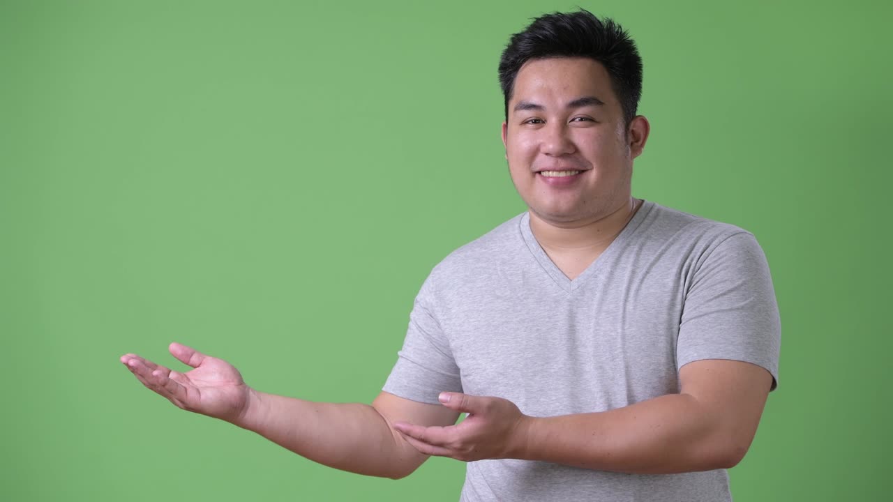 Young handsome overweight Asian man against green background