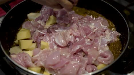 Diced Chicken And Potato Being Placed Into Saucepan With Simmering Curry Sauce