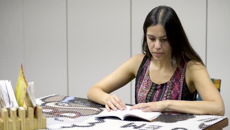 hermosa joven morena buscando información en un libro sentado en la mesa