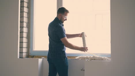 man applies spray foam on sill and girl with bucket in room