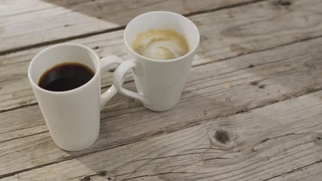 video of white cup of coffee with milk and cup of black coffee over wooden background