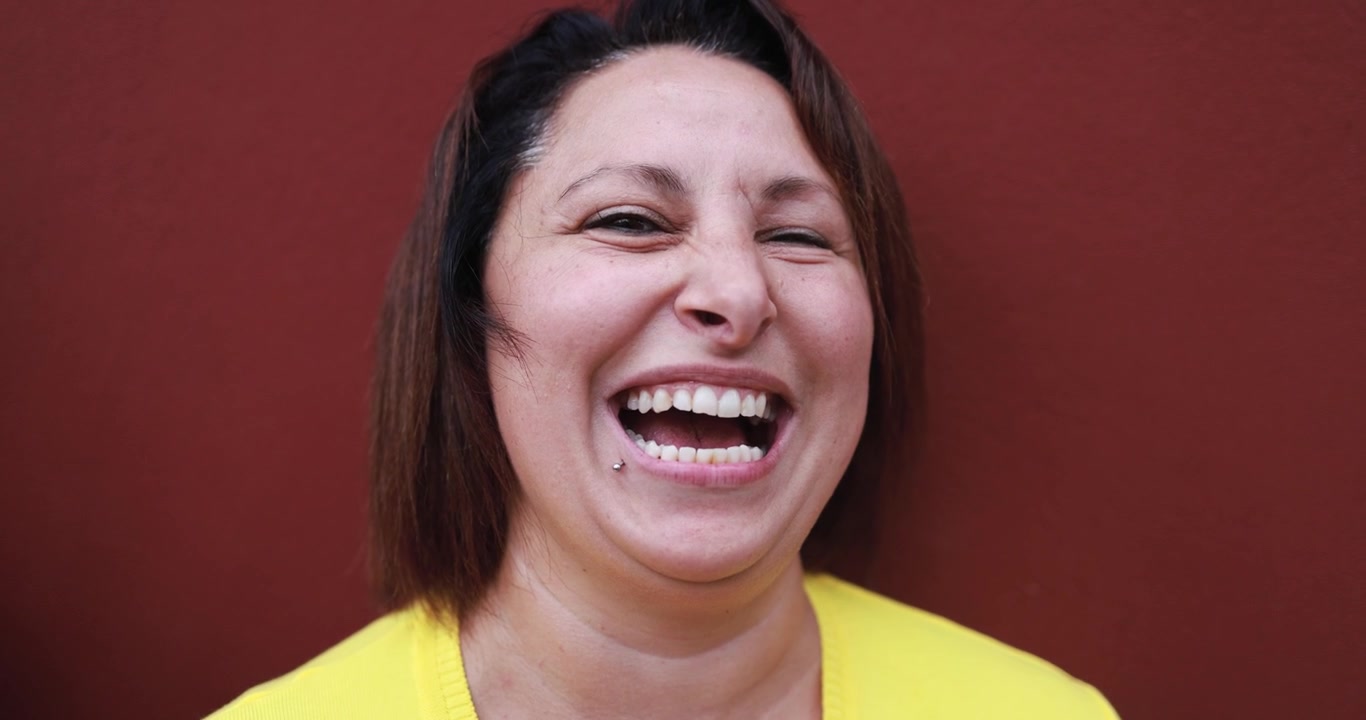 Donna di mezza età che ride gioiosamente contro un muro rosso