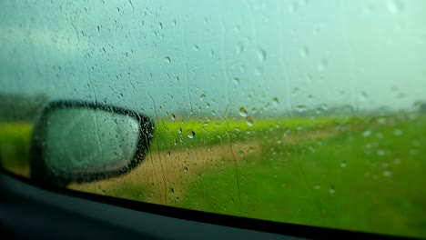 intense rainstorm viewed from inside the car, with raindrops cascading down the windshield and lush green fields beyond