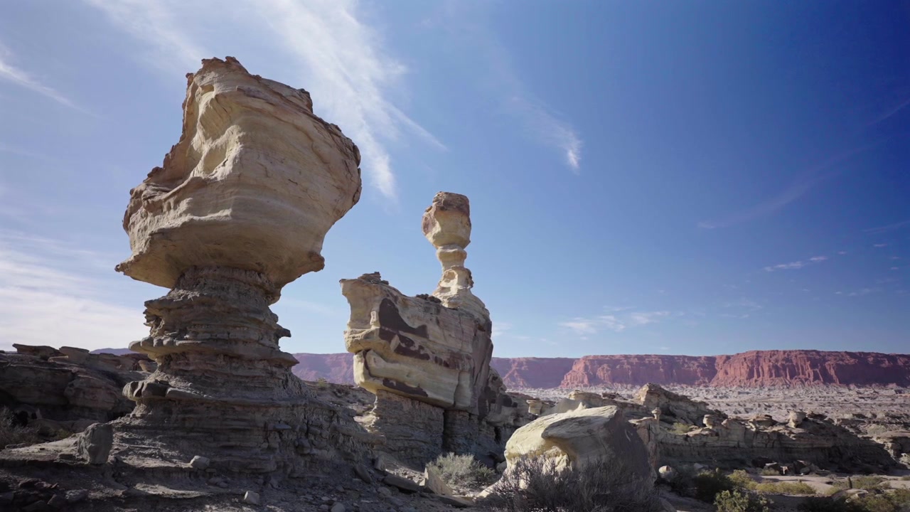 Arjantin'deki Ischigualasto Eyalet Parkı'nın kurak çöl manzarasında yer alan, yüksek, rüzgarla şekillenmiş kumtaşı kaya oluşumlarının çarpıcı gündüz çekimi. Berrak mavi gökyüzü ve engebeli araziler.