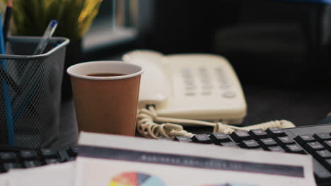 uma chávena de café e papelada na secretária do escritório, de perto.