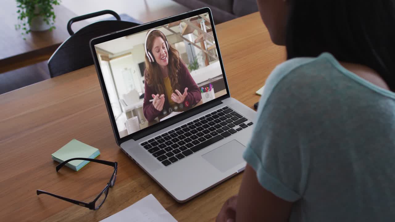 Mixed race businesswoman sitting at desk using laptop having video call with female colleague