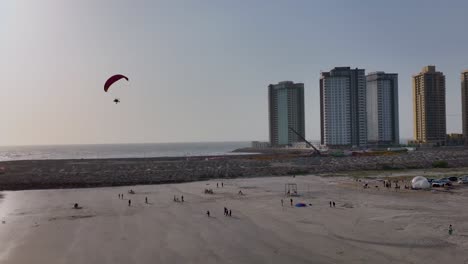 Aerial-Silhouette-Of-Paraglider-Flying-Over-Karachi-Beach-During-Sunset