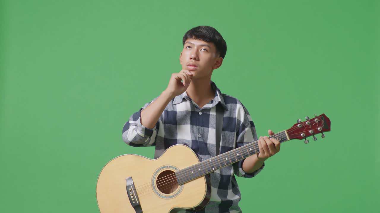 기타를 들고 있는 아시아 십대가 무언가를 생각하고 녹색 화면 배경에서 주변을 둘러보고 있다