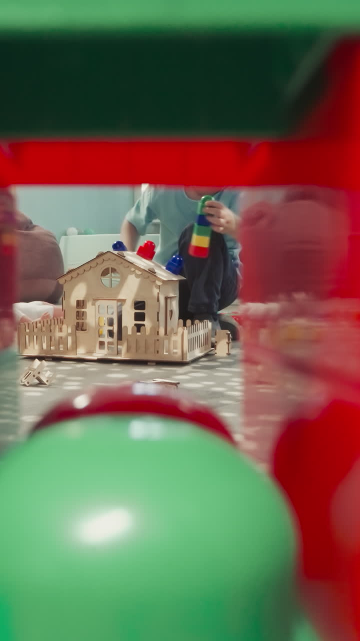 유아는 나무 집의 지붕에 다채로운 플라스틱 블록을 놓습니다. 귀여운 작은 소년은 거실에서 바닥에 앉아 큐브의 건설에서 클리어런스를 통해 볼 수 있습니다.