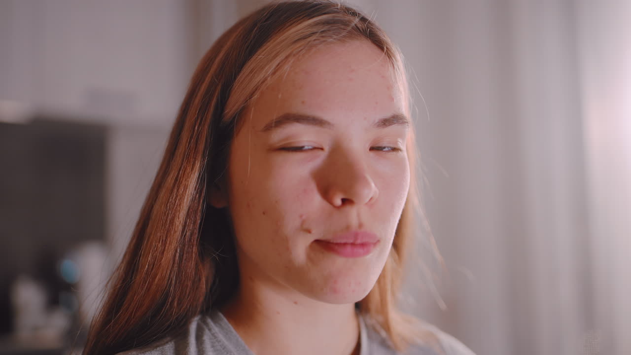 Close up of young woman in kitchen eating sliced cucumber with natural expression, face lit by soft indoor light, showing freshness and simplicity of casual healthy lifestyle moment