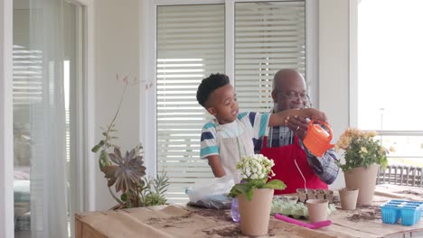 happy african american grandfather and grandson watering flowers on balcony, slow motion