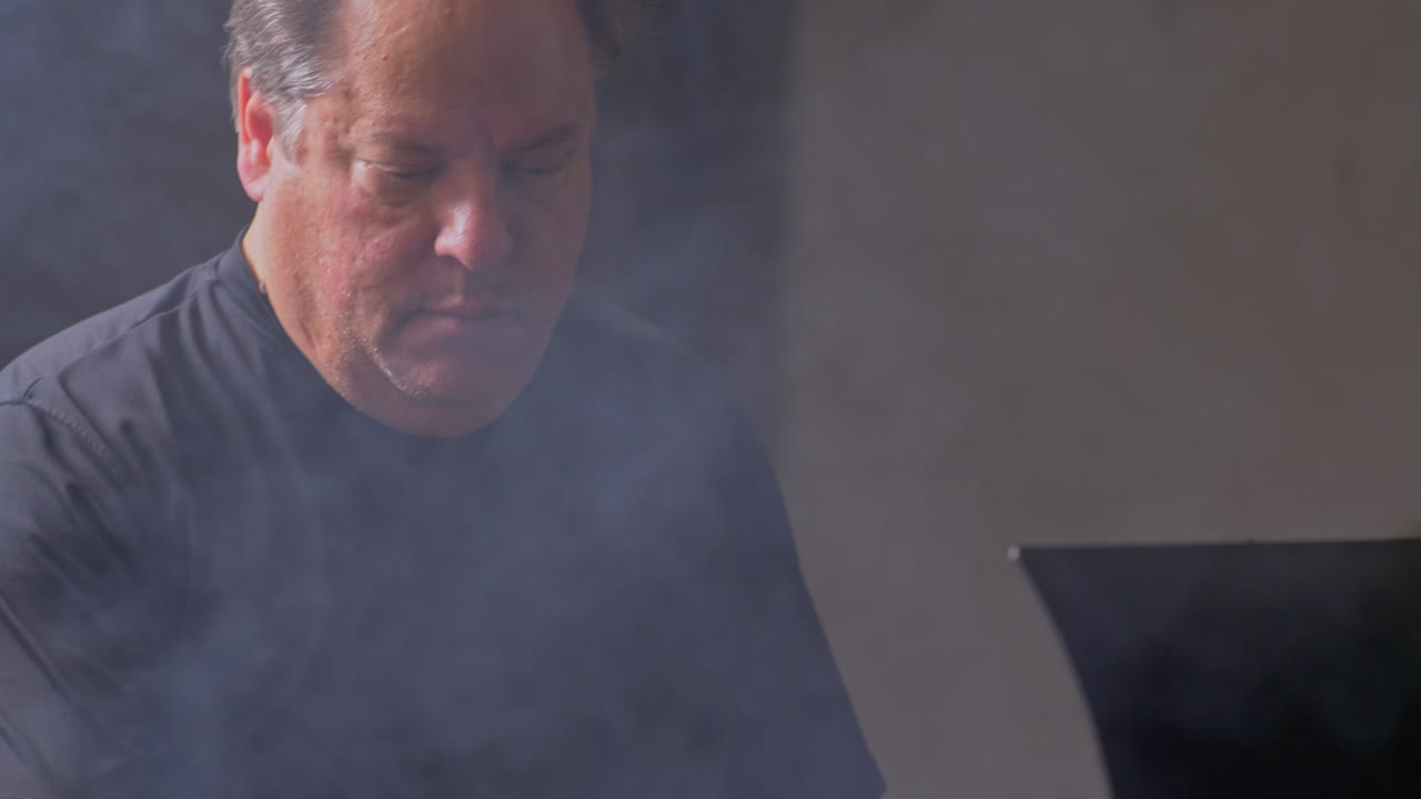 inclinarse hacia el hombre mientras el humo sale del pozo de la barbacoa