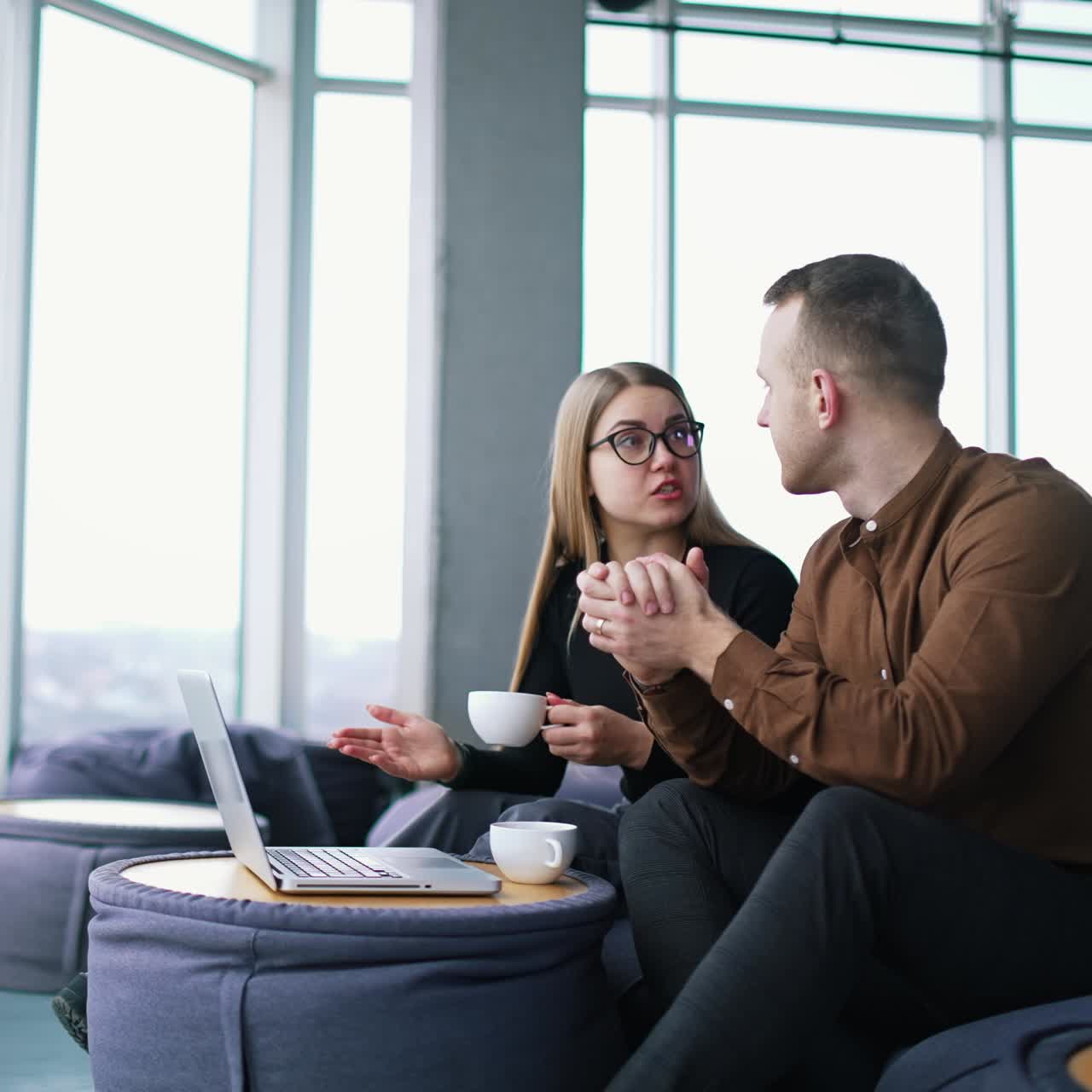Young business people talk in modern office. Handsome businessman and female partner sitting in comfortable chairs and having a conversation in front of a laptop