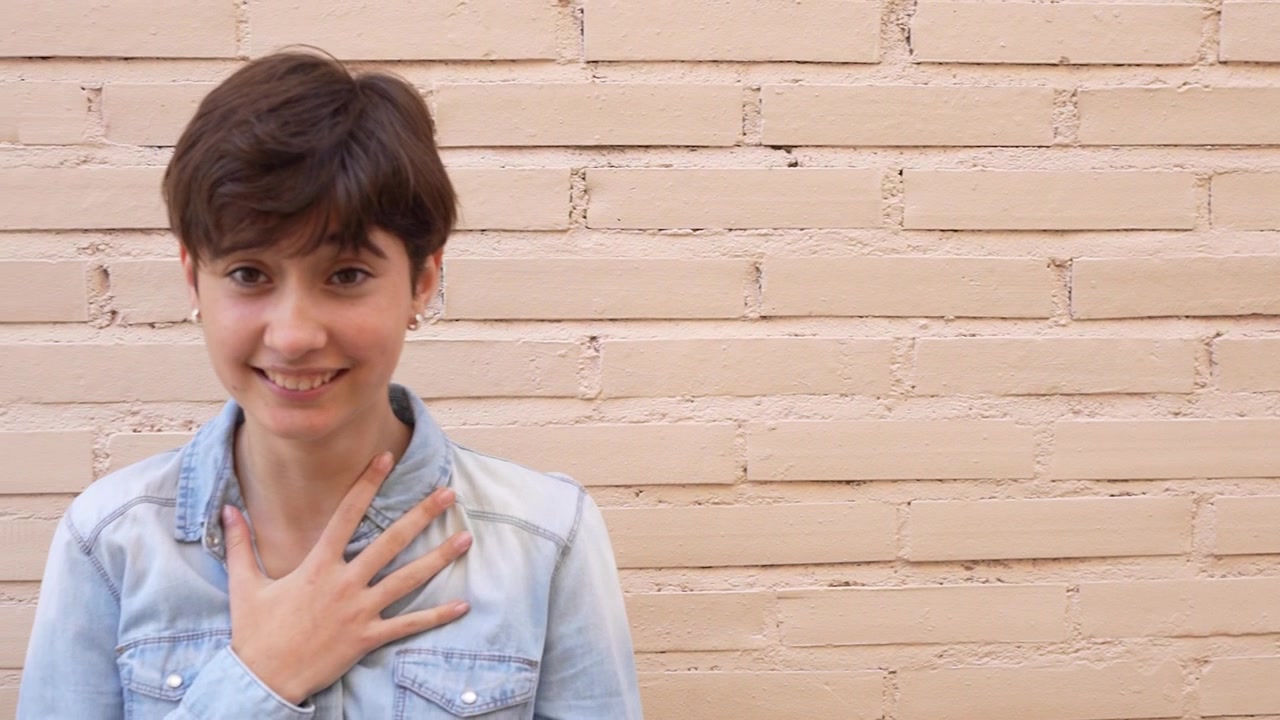 Un giovane sorride allegramente mentre si appoggia a un muro di mattoni texturizzato.